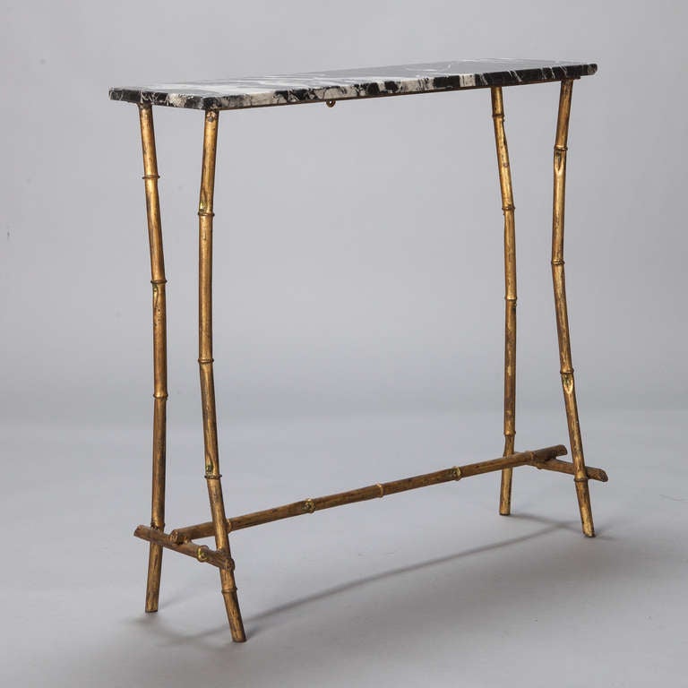 Circa 1940s small console table has a faux bamboo style frame with a gilded finish, and table top of black and white marble.