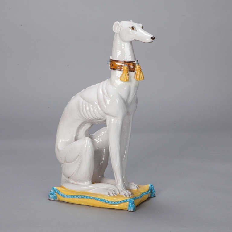 Circa 1950s porcelain statue of a seated greyhound in a white finish with a decorative, tassled collar.