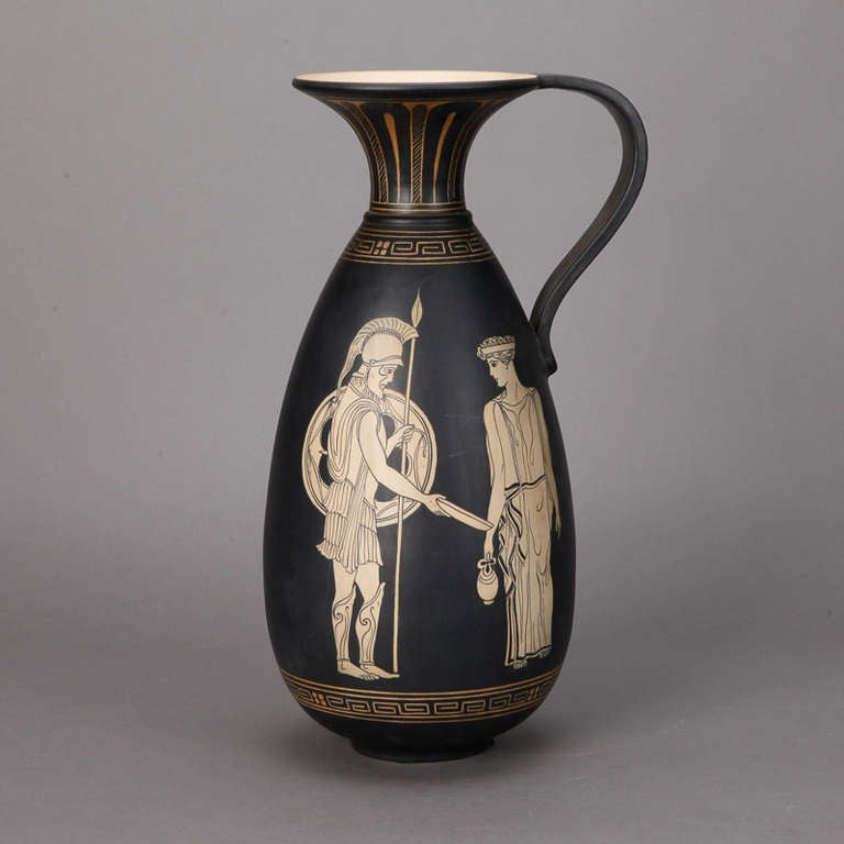Circa 1920's tall ewer with handle and classical figures on a matte black glaze with gilded details.