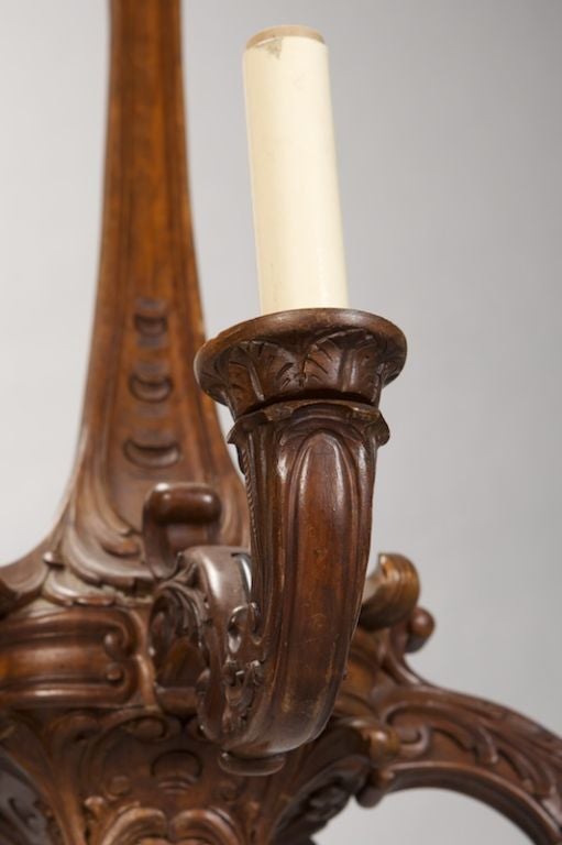 Circa 1860s four light carved walnut chandelier has been wired for US electrical standards. Square ceiling mount with intricate carved details, slender center shaft, four curved arms with carved foliate and scrolled details, large carved ornamental