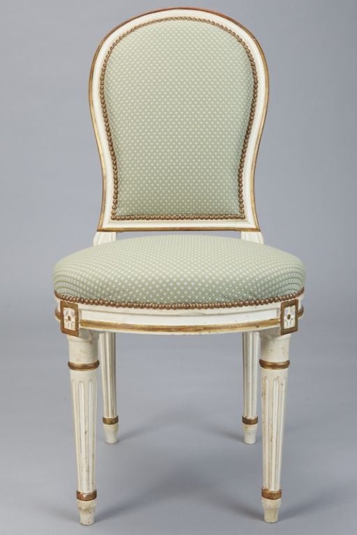Set of 8 Louis XVI style chairs with oval upholstered backs, creamy white painted and gilded wooden frames,  round upholstered seats, brass upholstery tacks, reeded legs. Newly upholstered in pale sage green fabric. All chair frames are solid, tight