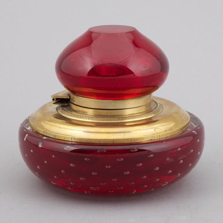 Round red glass inkwell with bubbles in the base, brass fittings, hinged lid and decorative glass top.
