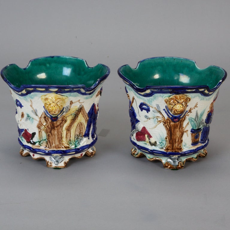 Pair of circa 1860's French footed majolica pots in blue, white and burgundy colored glaze with a motif of bulldogs, country cottages and children. Sold and priced as a pair.
