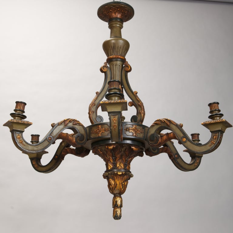 Circa 1930s French carved wood chandelier has six candle style lights. Painted finish in medium and dark olive green with gilded accents to highlight carved decorative elements including acanthus leaves, tassels, ridged bobeches and ceiling canopy.