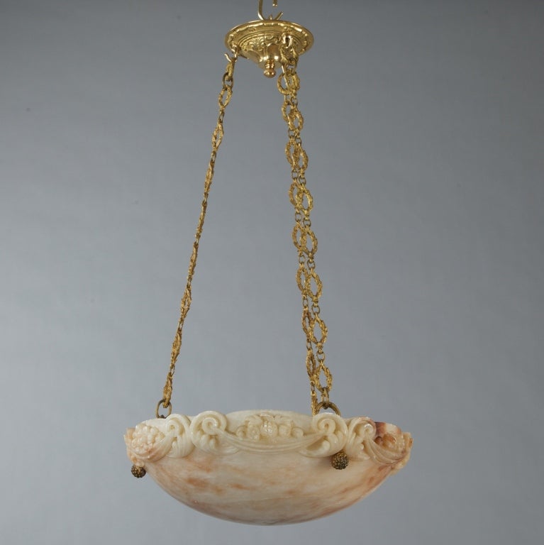Alabaster hanging light fixture with three internal light sockets and hand-carved border on the rim depicting scrolled acanthus leaves, draped bunting, fruit and flowers, circa 1900. Decorative cast brass chain with links in wreath form and polished