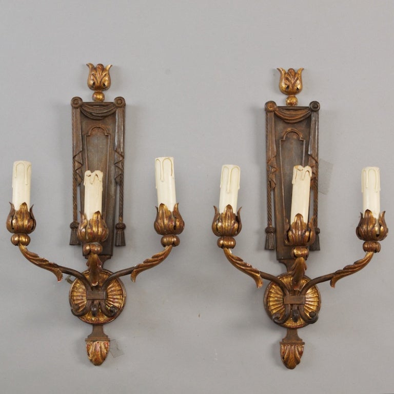 This pair of circa 1930 French three arm sconces are made of gilded metal with acanthus leaf crests, drapery and tassel design elements and acanthus leaf embellished bobeches. New wiring for US electrical standards. Sold and priced as a pair. 
