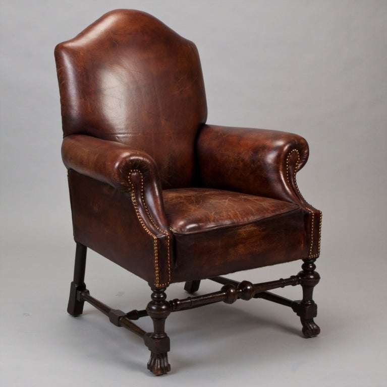 Handsome brown leather library chair with rolled arms, high curved setback, turned and carved wood legs and stretchers, brass nailhead trim. Seat is 19