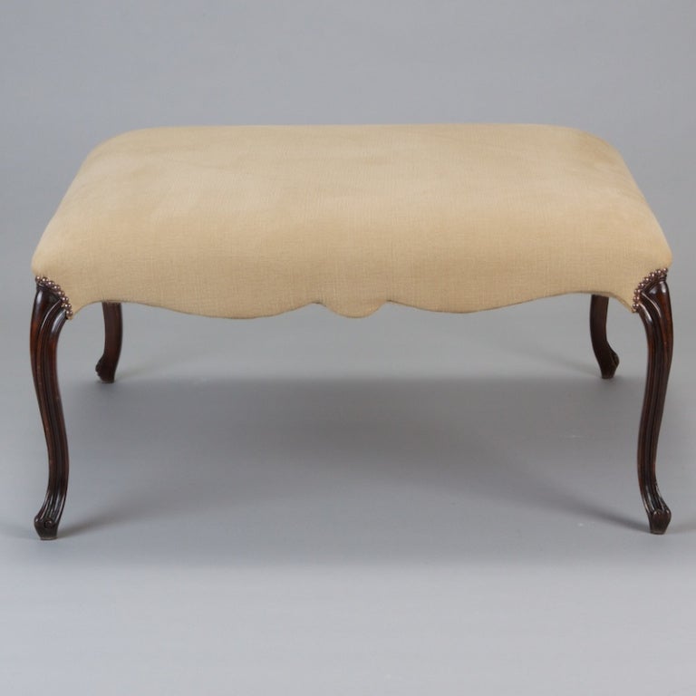 Classic square stool upholstered in neutral pale taupe fabric with 19th century French walnut chair legs and brass nail head tacks.