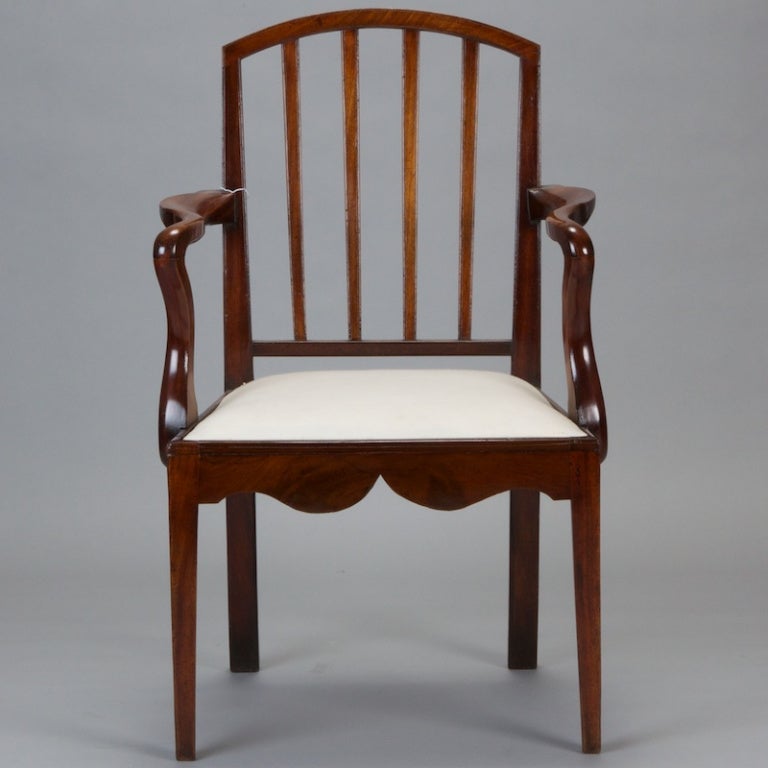 English armchair from Georgian period has polished wood frame with slatted seat back, curved arms, decoratively carved apron, upholstered seat and tapered front legs. Seat is 17.5