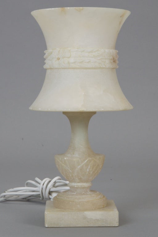 Found in France, this all alabaster lamp has a carved pedestal base and modified hour glass shaped shade with carved center floral and leaf garland. Rewired for US electrical standards. Base is 4-1/2
