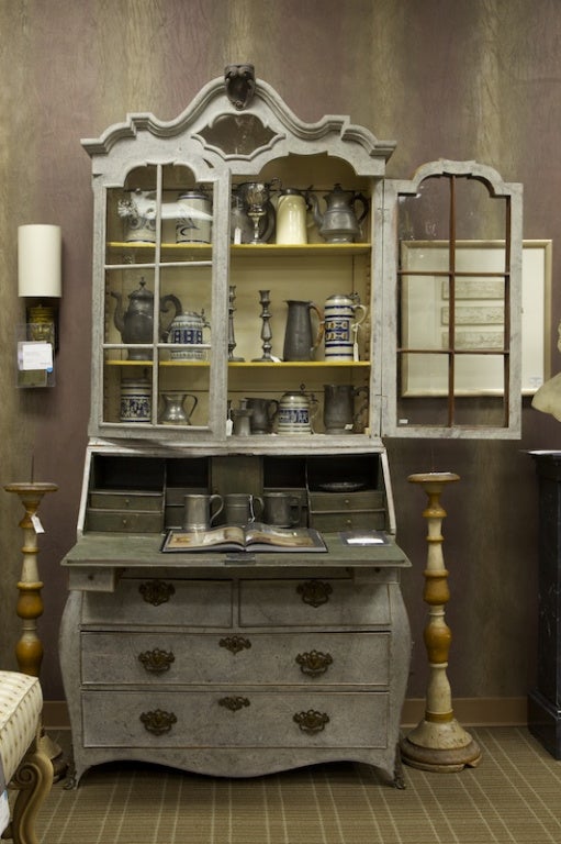 Tall late 18th century Swedish bureau bookcase with gray painted finish has top section with glass front doors, curvy crest and internal shelves. Drop down desk front has pull out supports below and four drawers with brass hardware.