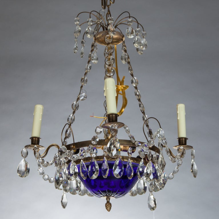 Suspended by chains, this late 19th century Swedish chandelier has a brilliant blue ceSuspendednter glass bowl, four candle style lights and large clear faceted crystals. We have three other similar Swedish chandeliers with blue glass centers. 