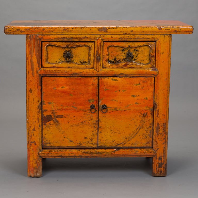 Chinese side cabinet has a worn yellow / orange lacquered finish with two functional drawers over two door compartment with internal shelf.