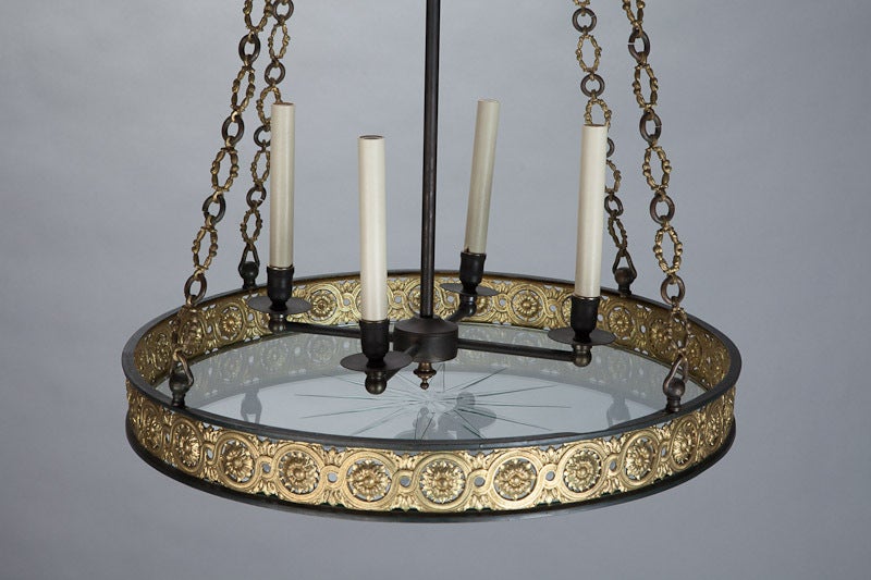 Unusual circa 1920s French hanging light fixture has a decorative canopy with cast brass open shell form crown and cast brass chain. Fixture base is a round black metal platter with a decorative cast brass rim of reticulated floral medallions in