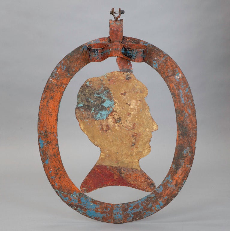 Found in England, this 19th century Folk Art piece started life as a hanging store sign. Painted metal oval frames a cut-out Silhouette of a male bust. Bow-shaped top piece with hanging hardware. Can be suspended or hung on a wall.
