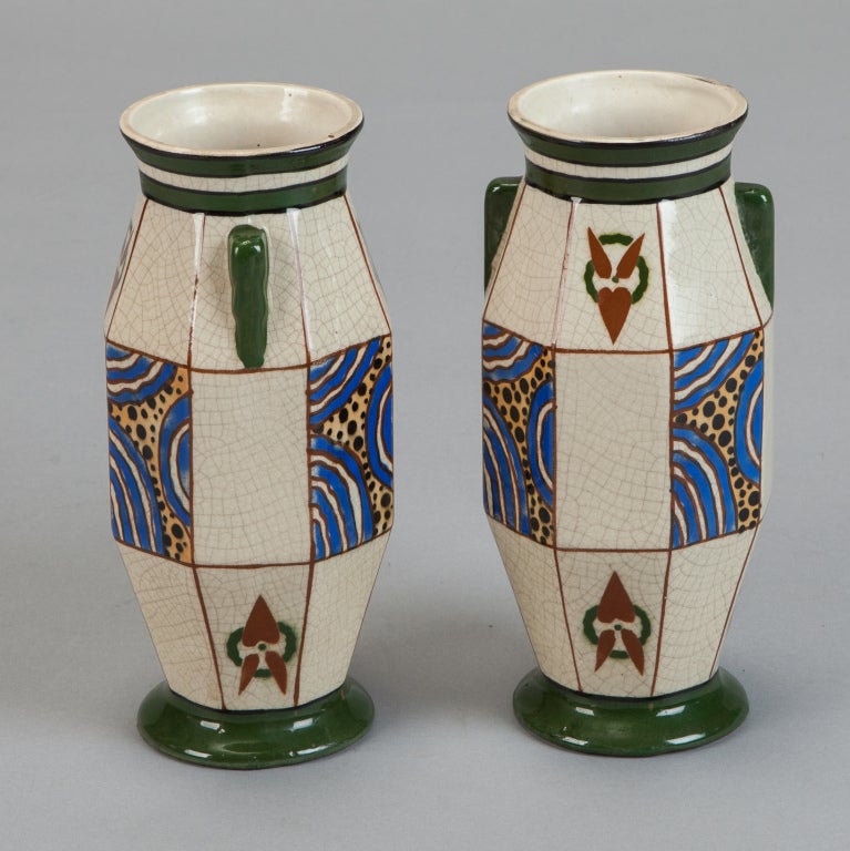 Pair of Deco-era vases by Auguste Mouzin et Cie (AMC) of Belgium. Ivory background with crazing and flat panels with abstract designs in royal blue, gold, green and rust. Applied handles, green bases. Marked on bottom. Sold and priced as a pair.