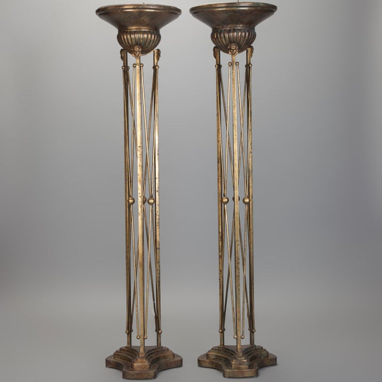 Pair of six foot tall iron floor lamps with bronze tone finish, stepped trefoil bases, columns of criss-crossing rods and beads with urn style bowls with sculpted faces embellishing the ridged base.  Up style lights newly wired for US electrical