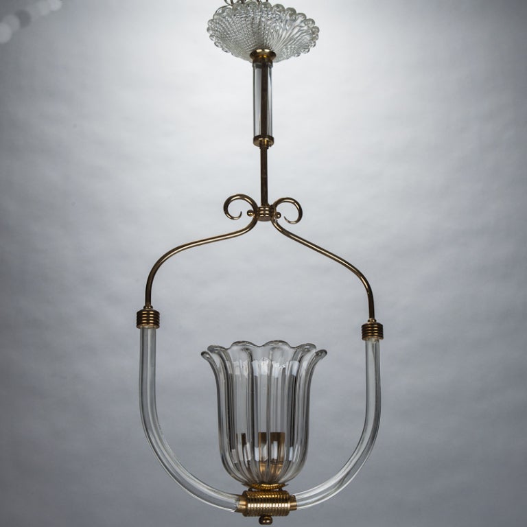 
Pendant fixture attributed to Barovier and Toso. Single light fixture has a handblown clear glass tulip form shade with candle style light. Light is suspended from center of a bird perch form consisting of clear handblown glass polished brass.