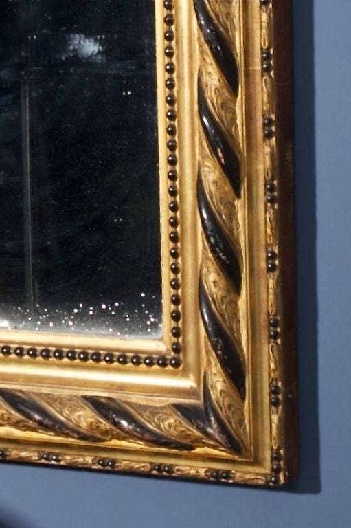This Louis Philippe style mirror features an elaborate gilt and ebonized frame. Original mercury mirror.  Actual Mirror Size:  49.5” h x 31.5” w