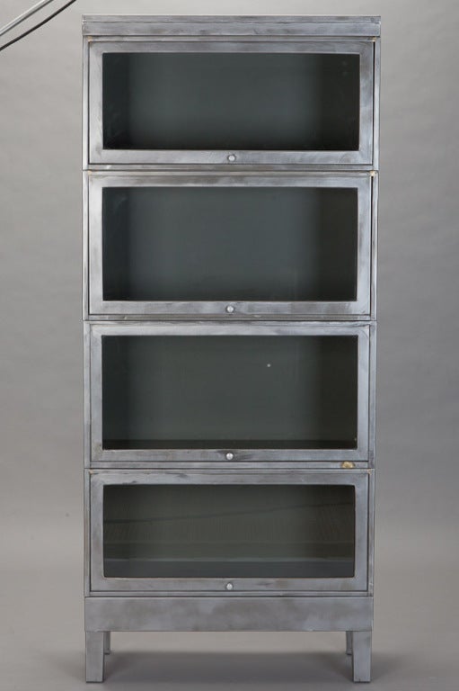 World War II era stacking metal bookcase has a footed base, top piece and four glass front compartments. From a US military base. Two available - sold and priced individually.