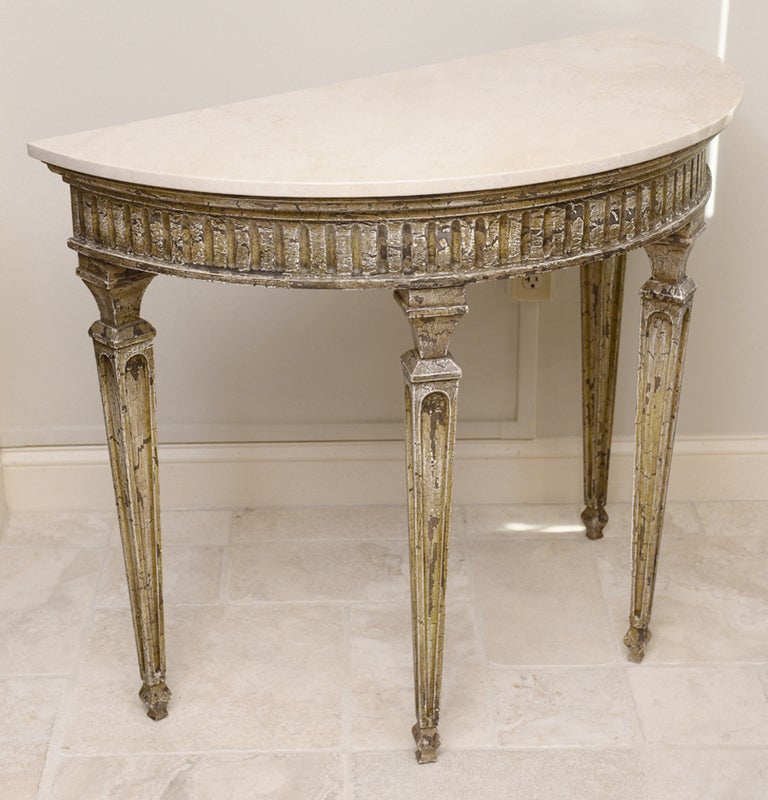 Demilune table, having distressed painted finish, creamy travertine top, on conforming fluted apron, raised on square tapering fielded legs.