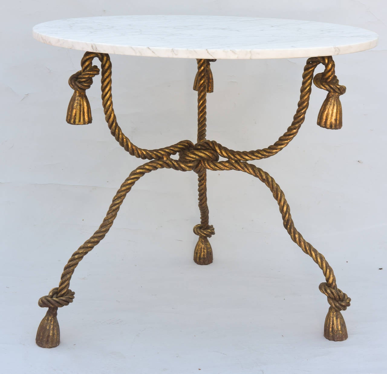 Occasional table, by Niccolini, having a round top of Carrara marble, on base of heavy gauge, gilded iron, formed as ropes, joined by a thick knotted stretcher, ending in knots and tassels.

Stock ID: D6338