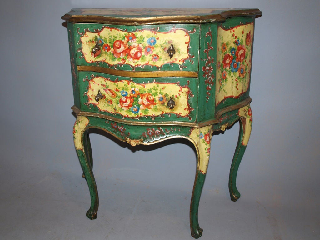 Polychromed Venetian commode, vibrantly handpainted with floral sprays surrounded by scrollwork, having a shaped serpentine top, above a conforming case fitted with two drawers, the drawers and sides all painted en suite, raised on cabriole legs