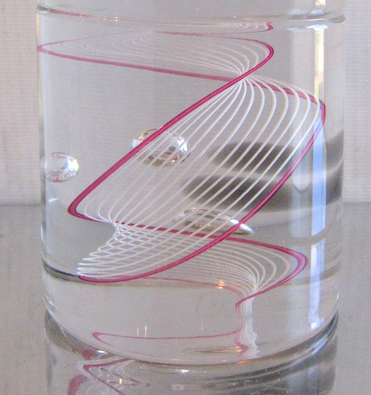 A Seguso for Oggetti tall cylindrical vase with white and vibrant pink cane in clear glass with 3 interior bubbles and 4 circular gray shadows.Signature is Etched Seguso A.V. for Oggetti. 

Oggetti are a luxury retailer of decorative home