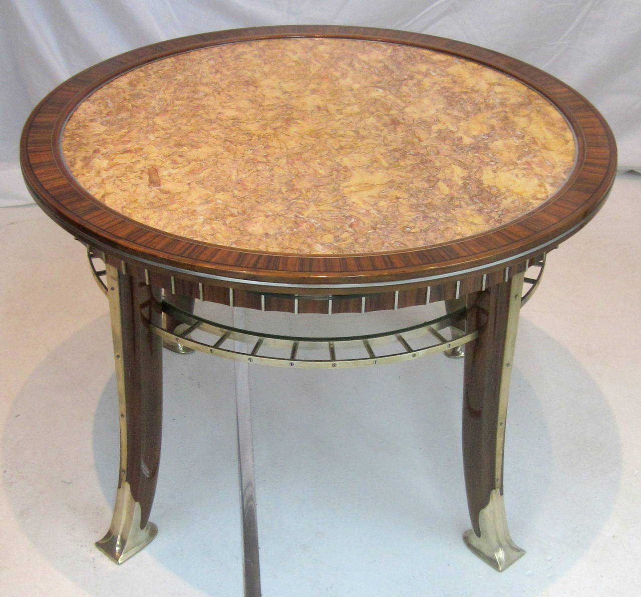 Si tratta di un tavolo da cocktail modernista Art Deco unico nel suo genere, con uno squisito piano in marmo del Belgio, legno di noce esotico e sabot e rifiniture in bronzo argentato. Il sottotavolo in vetro è straordinario, così come gli eleganti