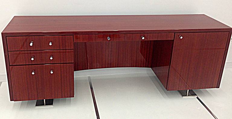 Single-sided desk with full modesty panel in makore veneer with high gloss finish, two pedestals, one with three drawers, the other, with shelves. Polished stainless steel feet. Polished chrome drawer pulls.
