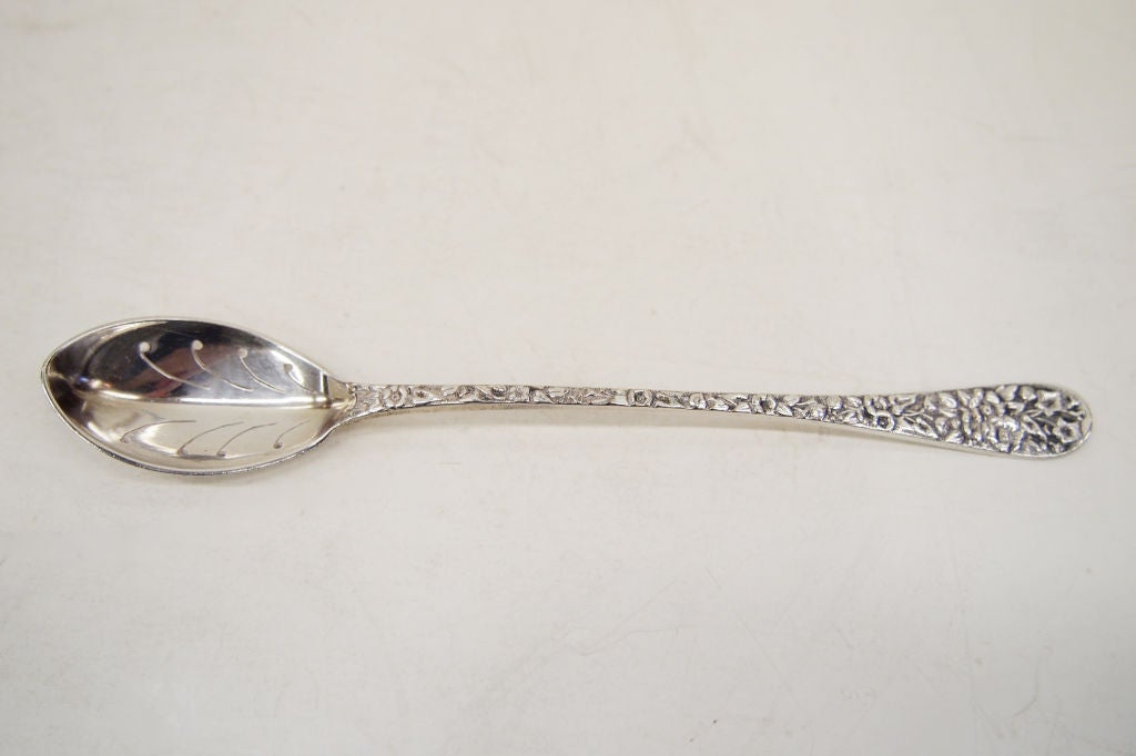 A Sterling Silver Oive Spoon with repousse floral decoration to front of handle.  Has monogram to top of back of the handle.  Weight 19 grams.  Patented 1894