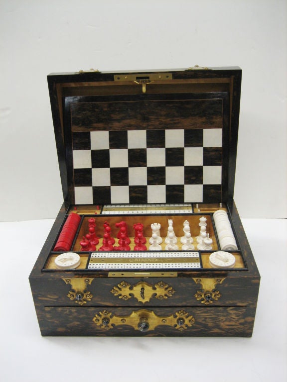 A handsome two drawer Games compendium featuring ivory chess set with board, cribbage board, draughts, bezique and dominoes.  Along with ivory tumblers and dice.  The whole in a macassor ebony and satinwood inlaid box set with agates in brass