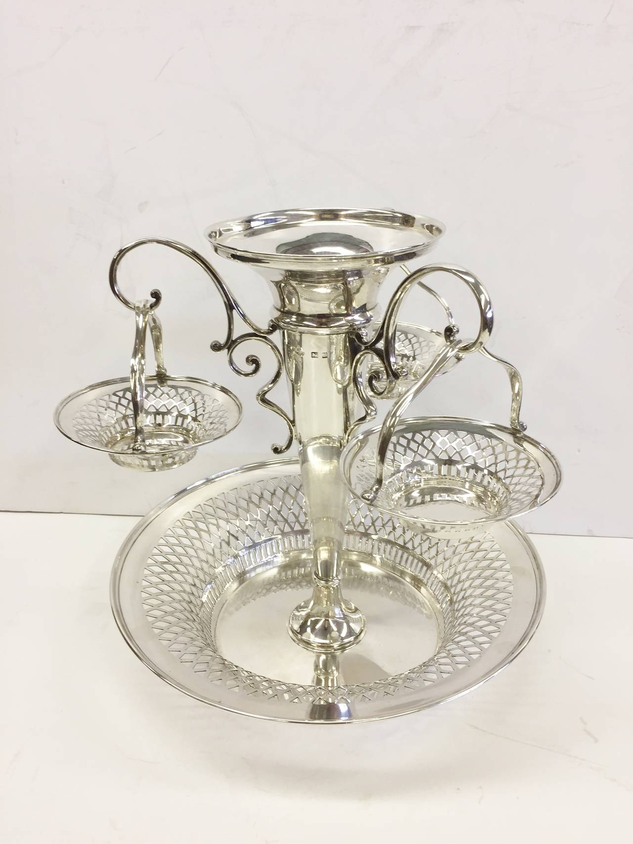 A fine dining table decoration in sterling silver. This epergne has three pierced hanging baskets and a removable pierced top bowl. The maker is the famous designer/silversmith Hukin and Heath. It was assayed in Birmingham, England in 1908.