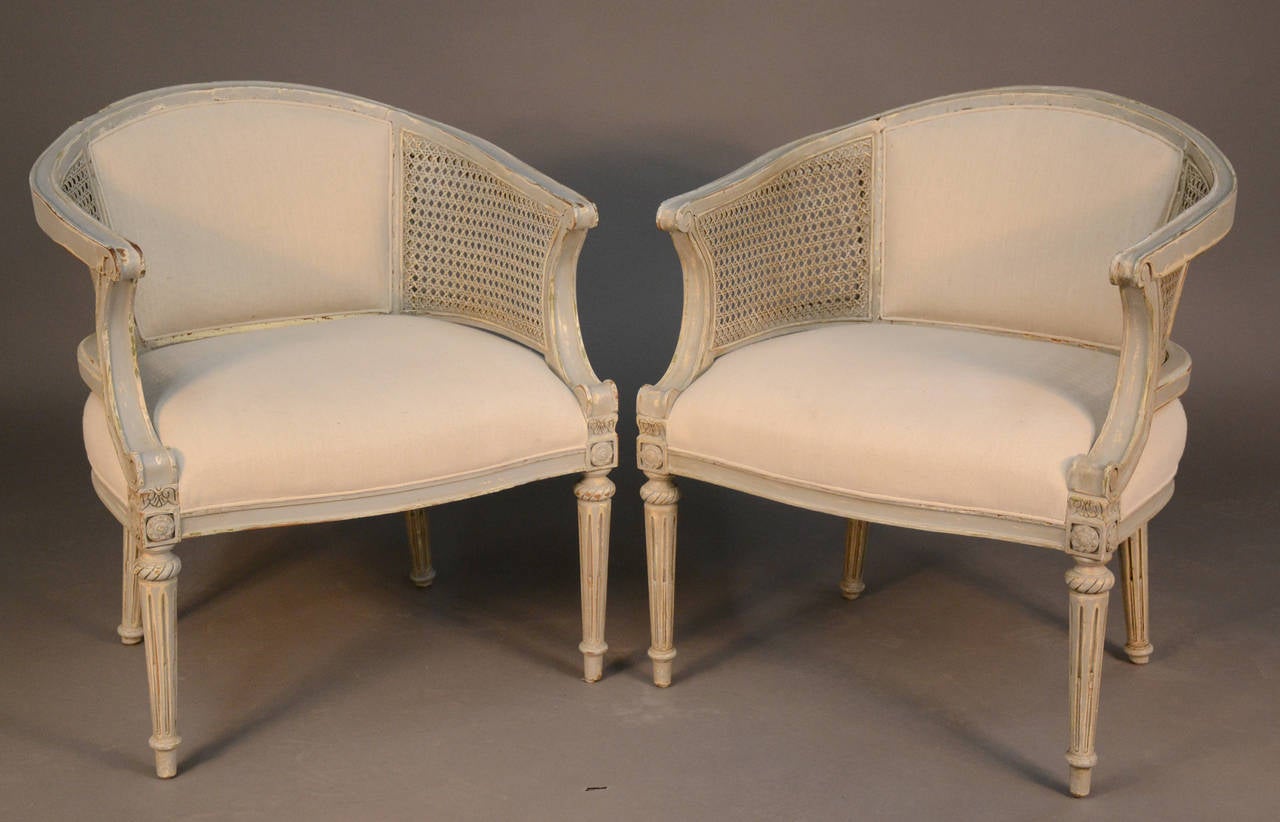 Pair of Louis XVI style grey patinated chairs with caned sides and upholstered back and seat in off-white linen and textured natural toned fabric on the back. With a sophisticated town and country versatility, the chic pair of chairs can work in a
