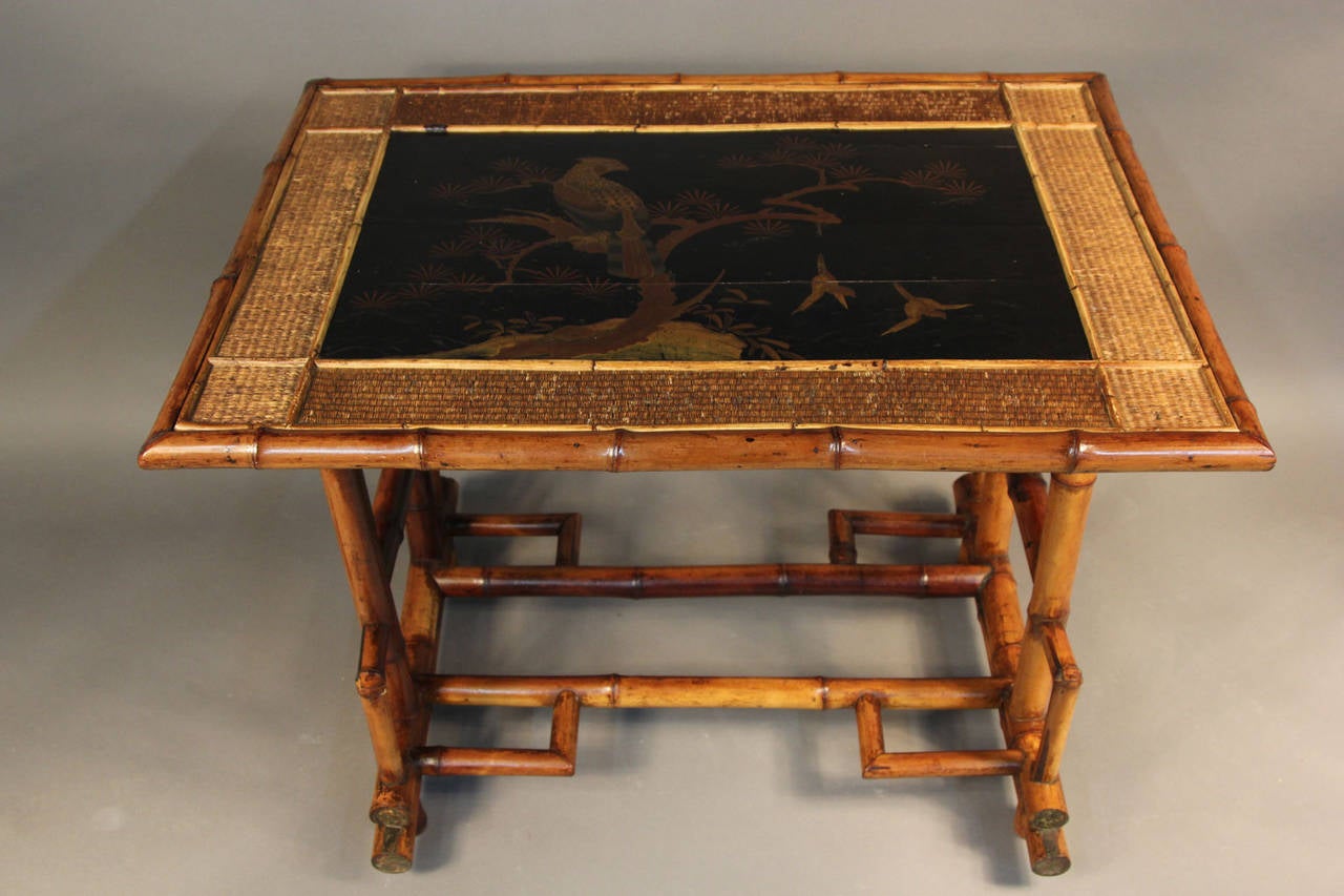 Bamboo construction.  The rectangular top with wicker surround and a central lacquered panel in the Japanese manner depicting an eagle and song birds.  Raised on an angled Oriental style base with stepped elements.