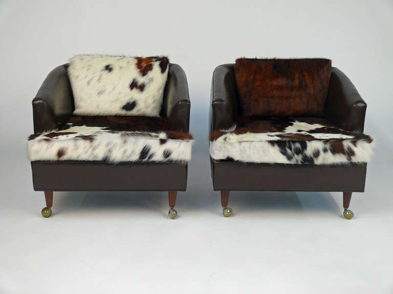 Pair of brown leather club chairs on rolling castors.  Mid century style, vintage from the 1960s.  Brand newly upholstered in authentic cow hide leather.  Removable back and seat cushions.