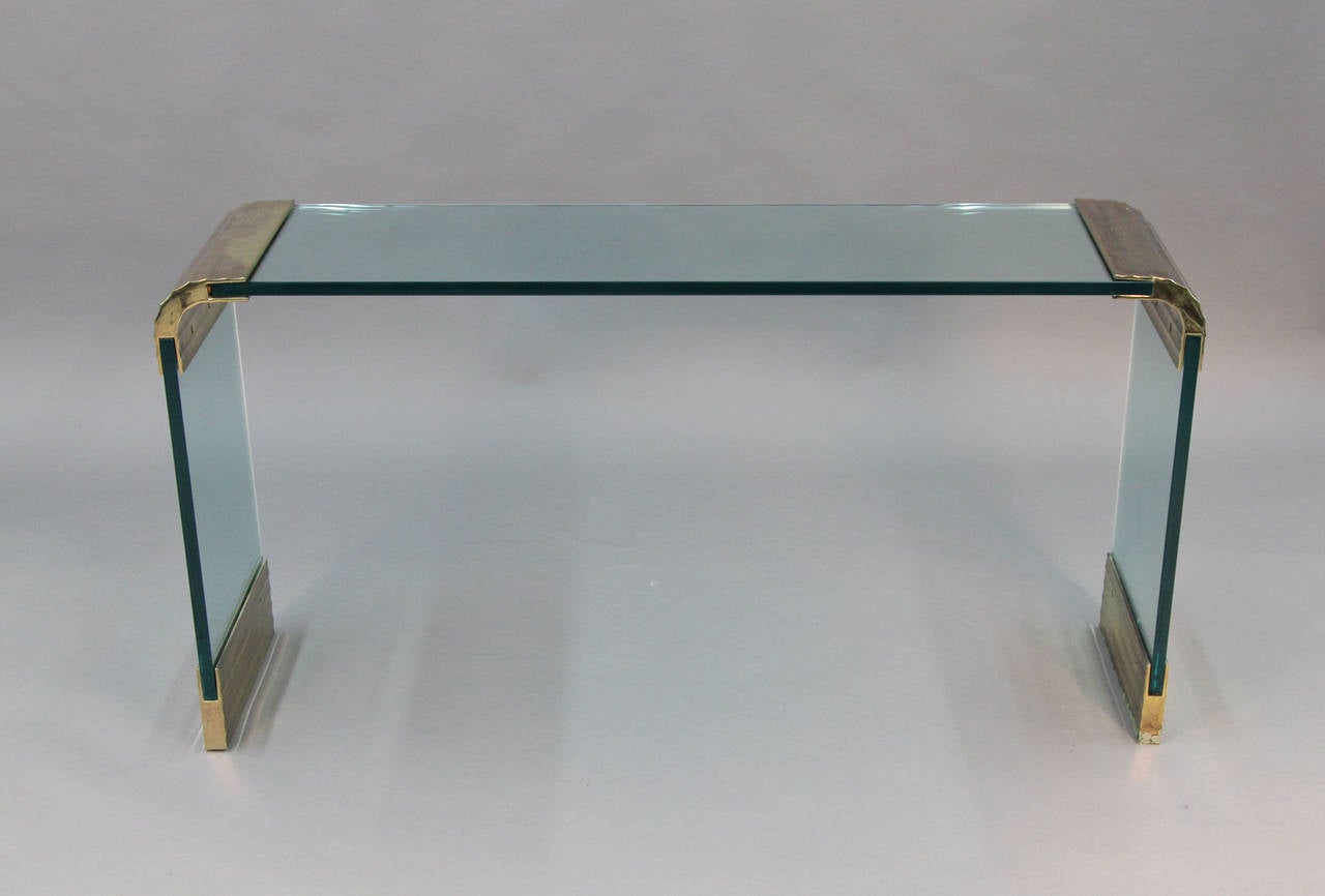 Thick Glass console with scalloped brass corners and brass feet.  Nice brass patina, small crack to back of one glass section.  Green patina to bottom of one brass foot.