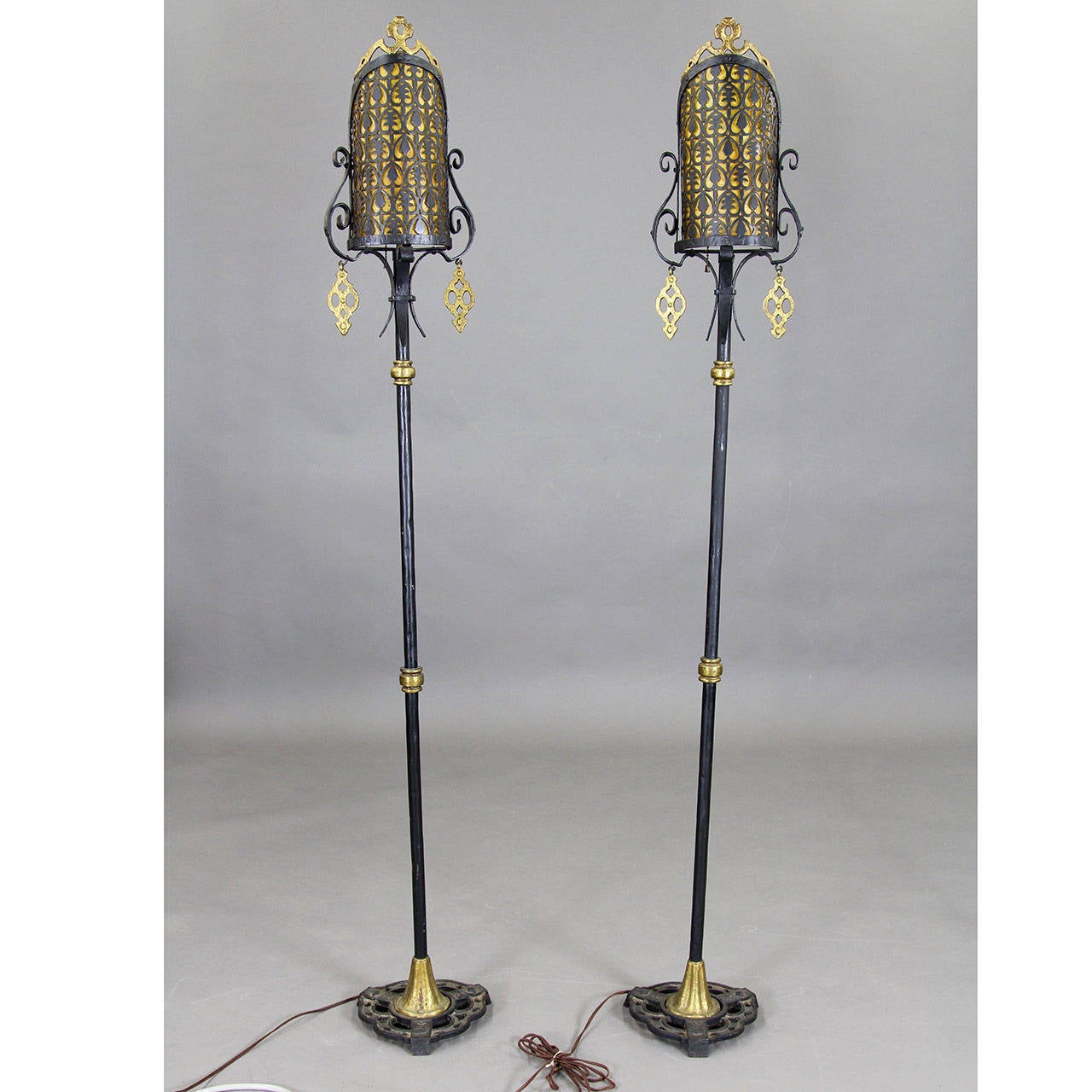 Early 20th century wrought iron floor lamps or torchieres, Art Deco design I the manner of Oscar Bach. Excellent condition with original celluloid shade lines in a golden pearl.