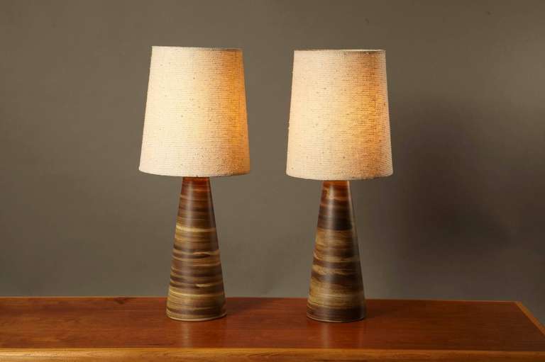Pair of brushed swirl glaze lamps and shades by Jane and Gordon Martz of Marshall Studios. The colors are dark brown matte over a light gray/brown. The stoneware body up to the walnut neck of these lamps is 14.5” tall x 6” diameter at the bottom. 3”
