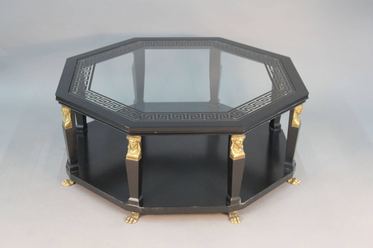 Unique and gorgeous Baker signed coffee table. Brass sphinx details on all legs. Black painted octagonal table with Greek key design on glass top.