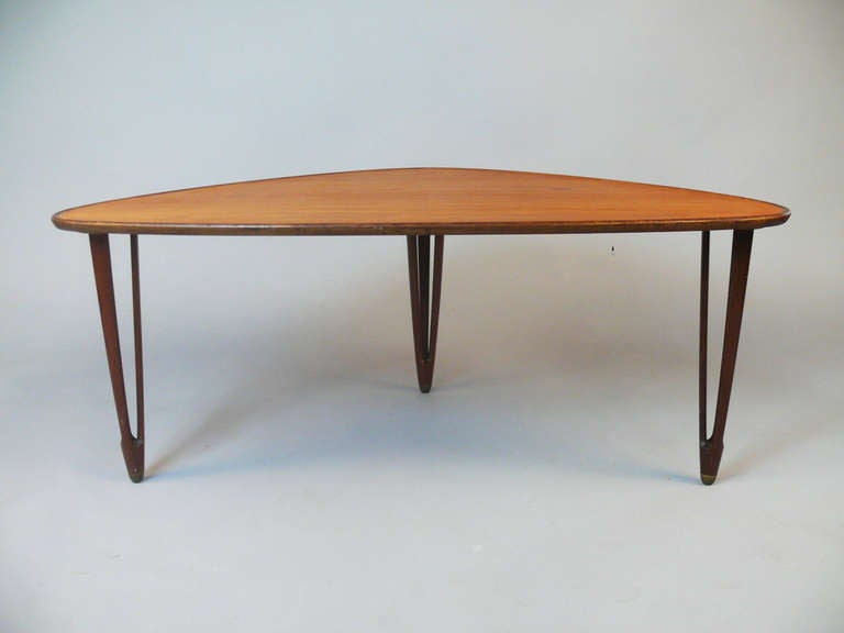Triangular, teak coffee table. Top with raised edge. Triple-split legs with brass leg caps. Produced by BC Møbler