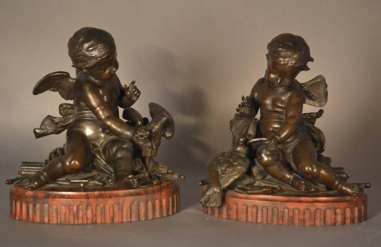 A fine pair of figural sculptures; each in the form of a patinated bronze cherub or putti with dove, raised on an oval red Griotte marble base. One depicting cherub composing a “Love” note with dove on-looking and second receiving and un-tying note