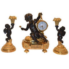 A Small Louis XVI Style Three Piece Clock Set with a Putto Playing a Drum