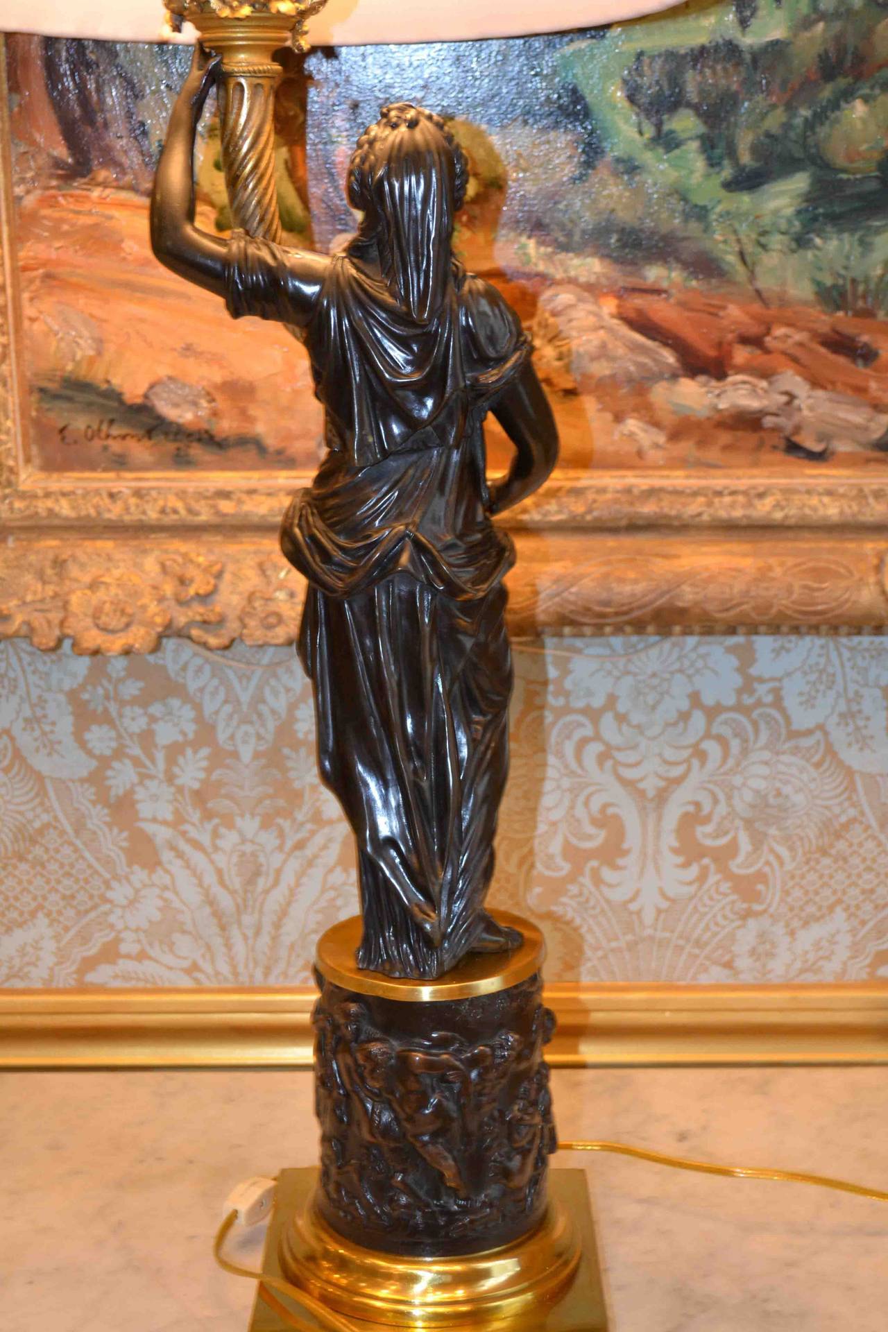 A standing classically draped female figure in finely chased patinated bronze, after a model by the French 18thC sculptor Clodion; she holds aloft a gilded cornucopia, (from which the statue has been wired); she stands on a circular bronze drum