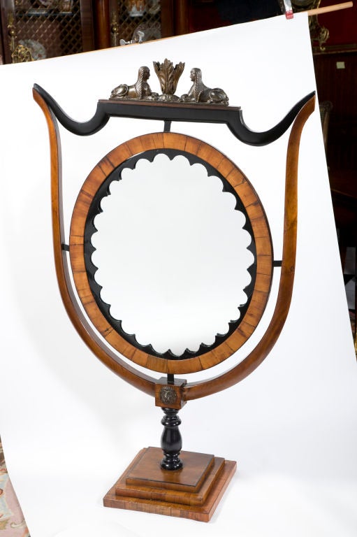 A rare and unusual example of a Viennese Biedermeier standing mirror in ebony and fruitwood.  The shield shaped frame supports an oval mirror surmounted by two facing ebonized Egyptian sphynx.  The whole on a stepped rectangular base.