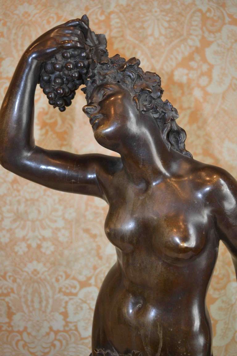 A brown patinated bronze allegorical statue of a nude bacchante, the roman goddess of wine, with right hand raised and holding a bunch of grapes, while the other rests on a trunk of an ancient vine.  Likely cast by one of the major Paris foundry's
