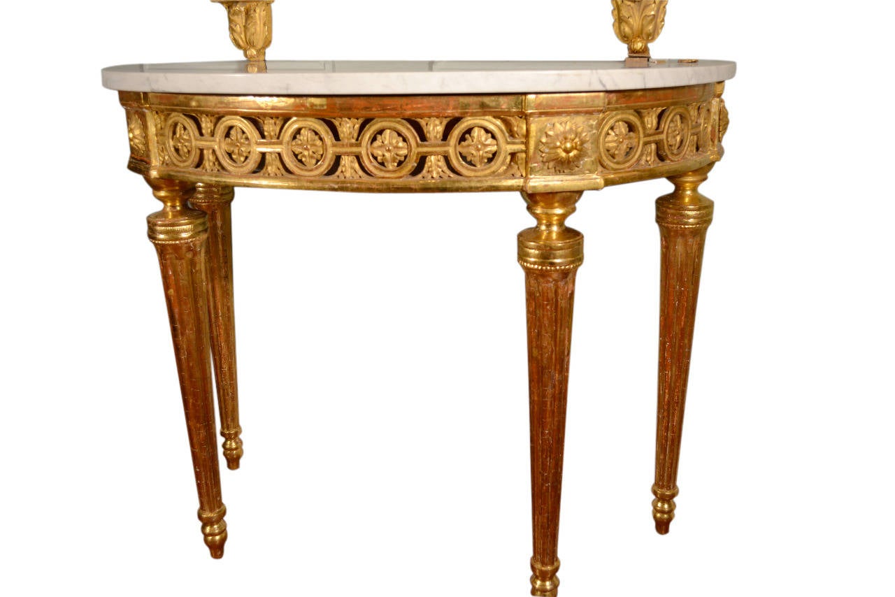 A spectacular and imposing gilded wood demilune shaped console table with a white marble top; on which is supported a tall gilded wood mirror, the rectangular frame with gilded rosettes to the corners; the mirror with a large gilded flower based