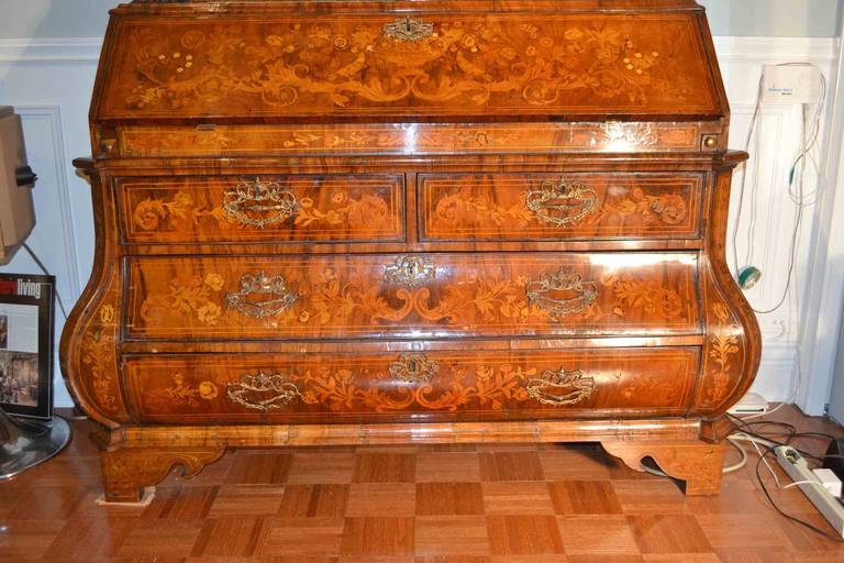 A 18th century Dutch marquetry desk and display case in overall floral marquetry; the arched molded cornice surmounted with a cartouche, above a pair of glazed doors fronting an upholstered shelved interior; with four drawers in the bombe lower