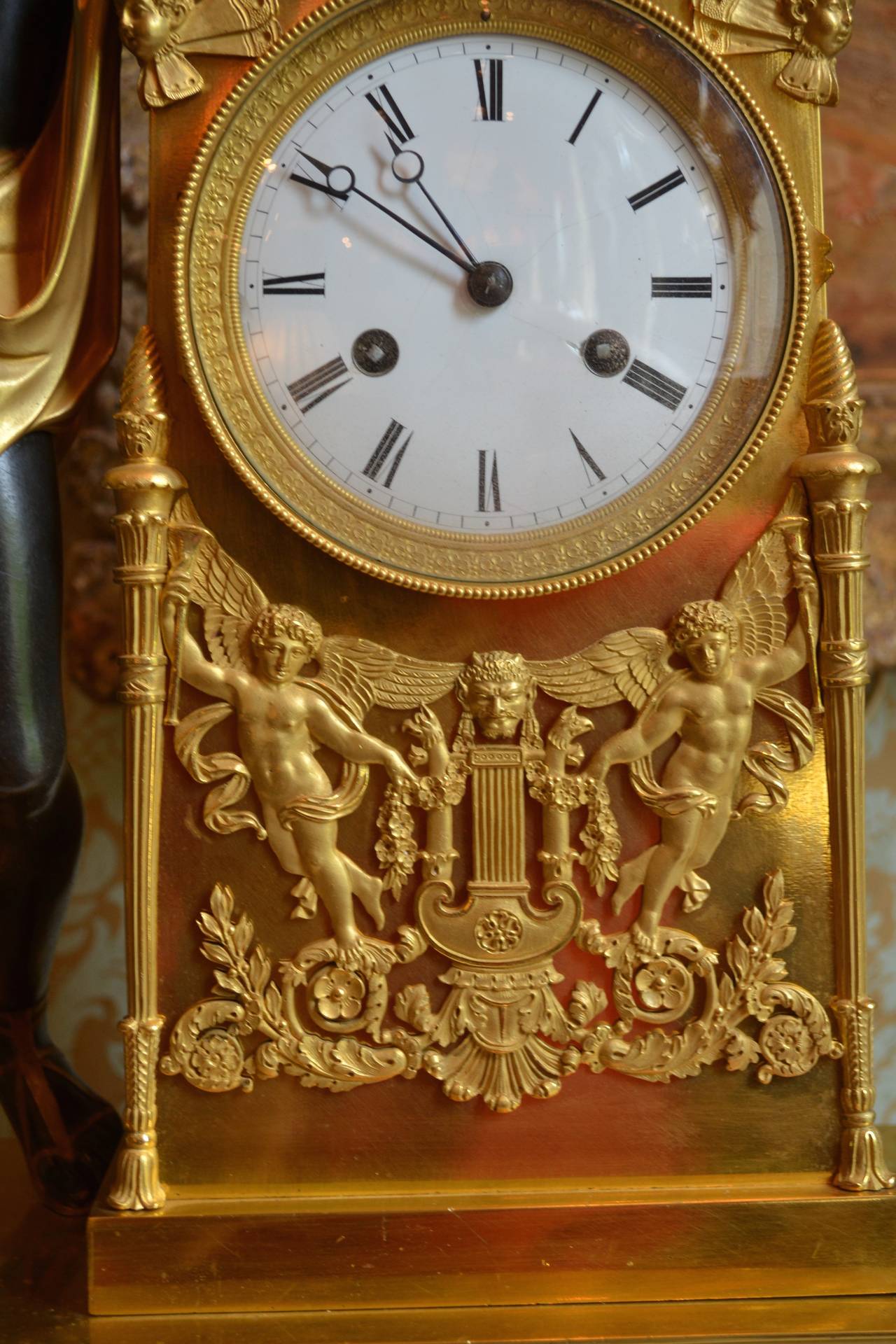 A fine and rare model first Empire Napoleonic mantel clock in gilded and patinated bronze. The patinated standing figure of Apollo is draped with a gilded sash over his shoulder; he holds and plays a gilded lyre in his arms, one of which rests on