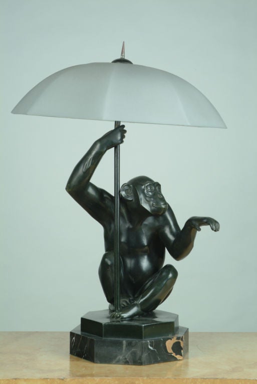 A dark green patinated bronze seated monkey holding a frosted glass umbrella with one hand, and testing for rain with the other hand, on a black marble base, French early 20thC; signed Le Verrier;